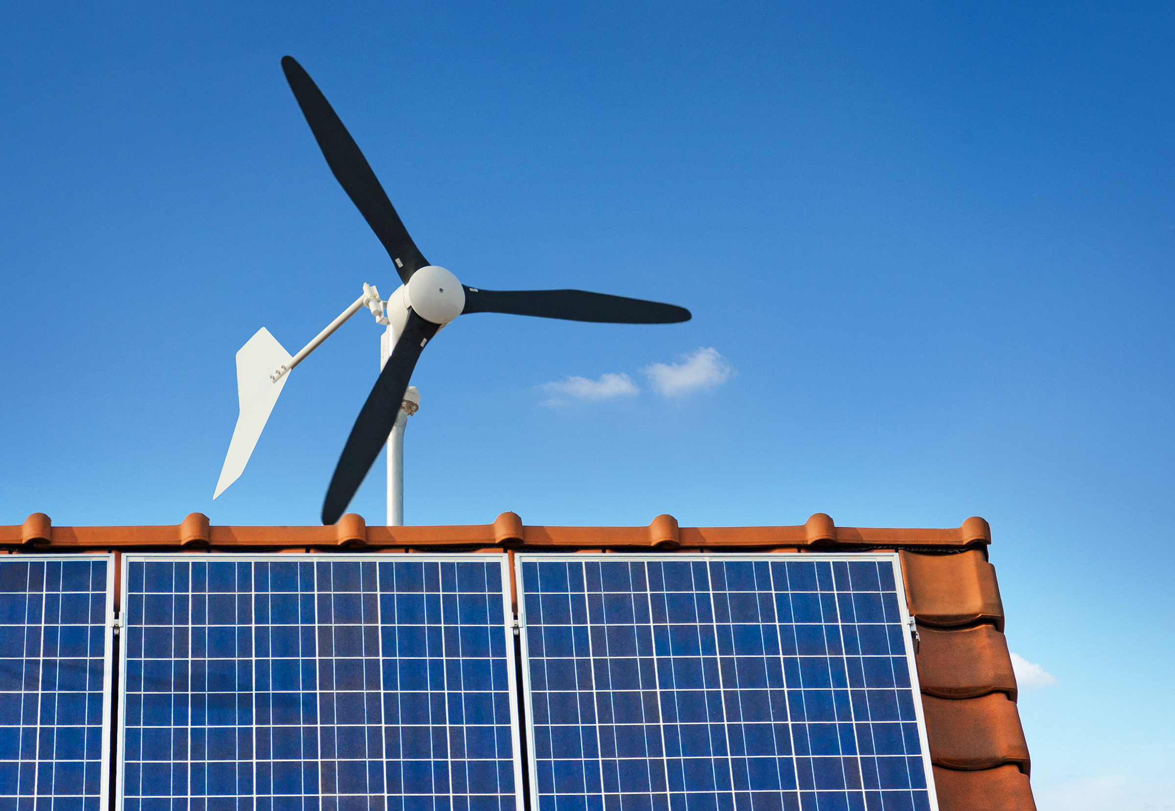 Eine Kleinwindkraftanlage und Solarmodule auf einem Dach erzeugen Strom