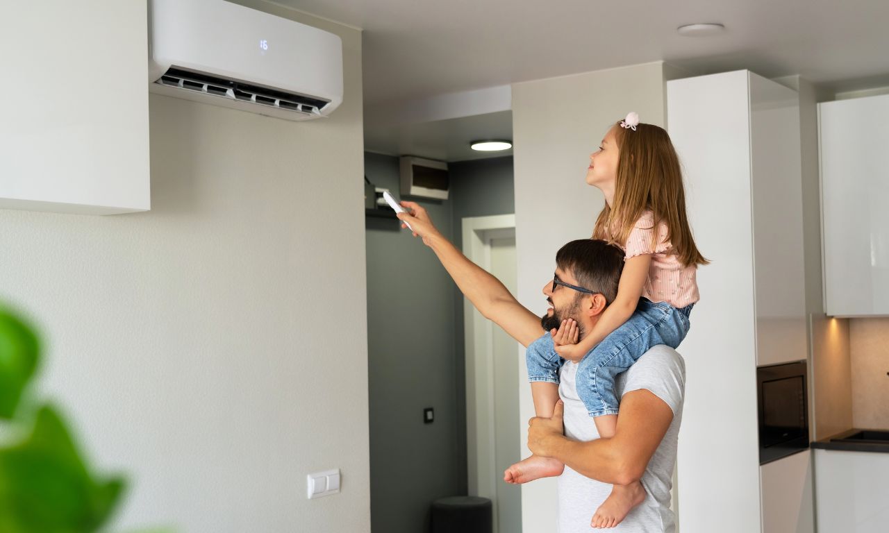Ein Vater mit kleiner Tochter auf der Schulter schaltet fröhlich seine Klimaanlage im Haus an.