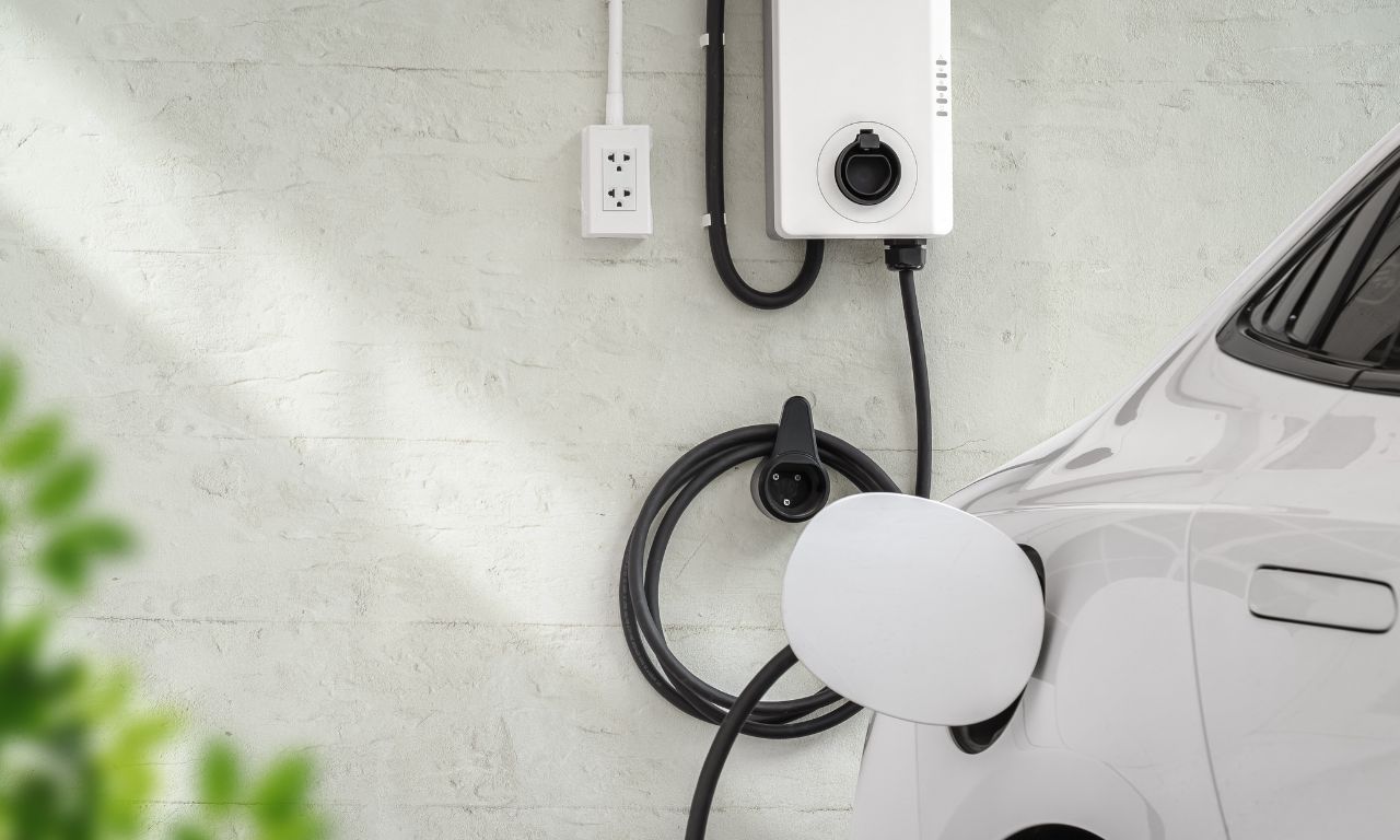 Weiße Wallbox hängt an der Wand, ein weißes E-Auto wird geladen.