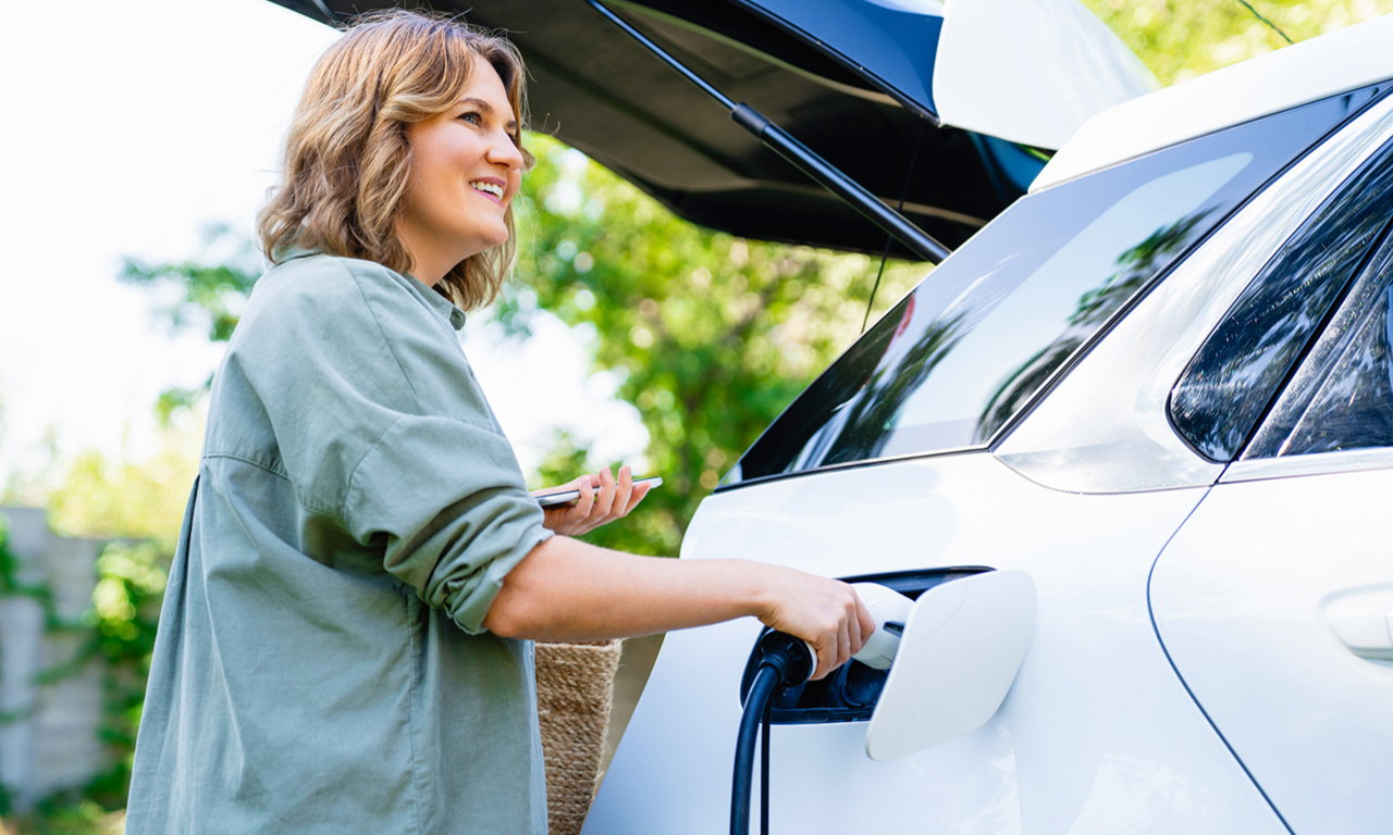 Eine Frau lädt glücklich ihr weißes Elektroauto.